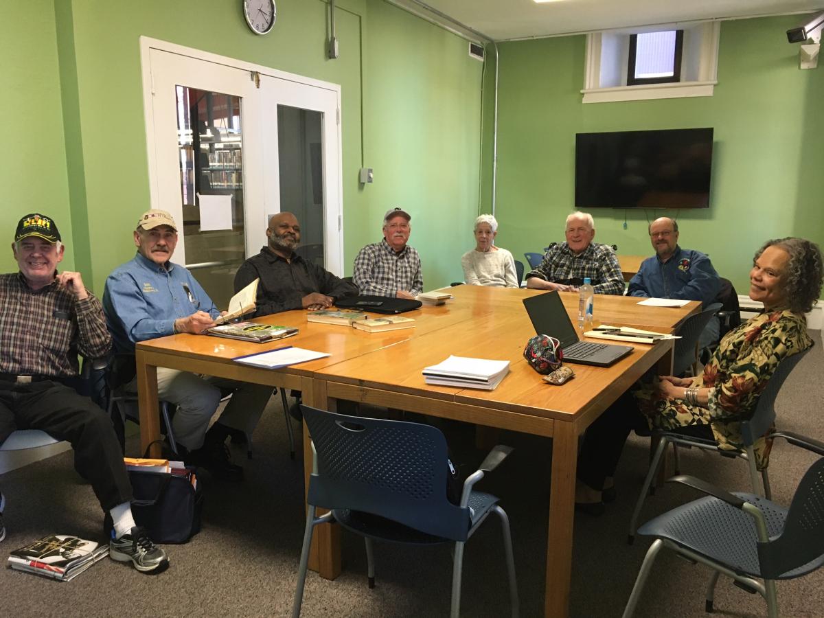 Men and women Veterans sitting around a broad wooden table, working on writing prompts.